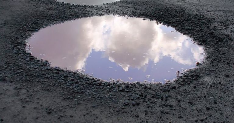 Pothole filled with water, reflecting a blue sky.